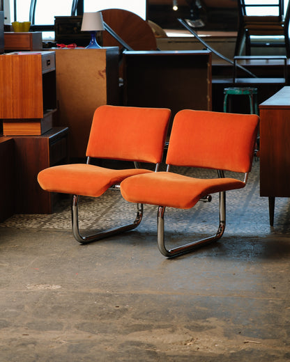 Pair of orange tubular chairs staged in a vintage furniture showroom.