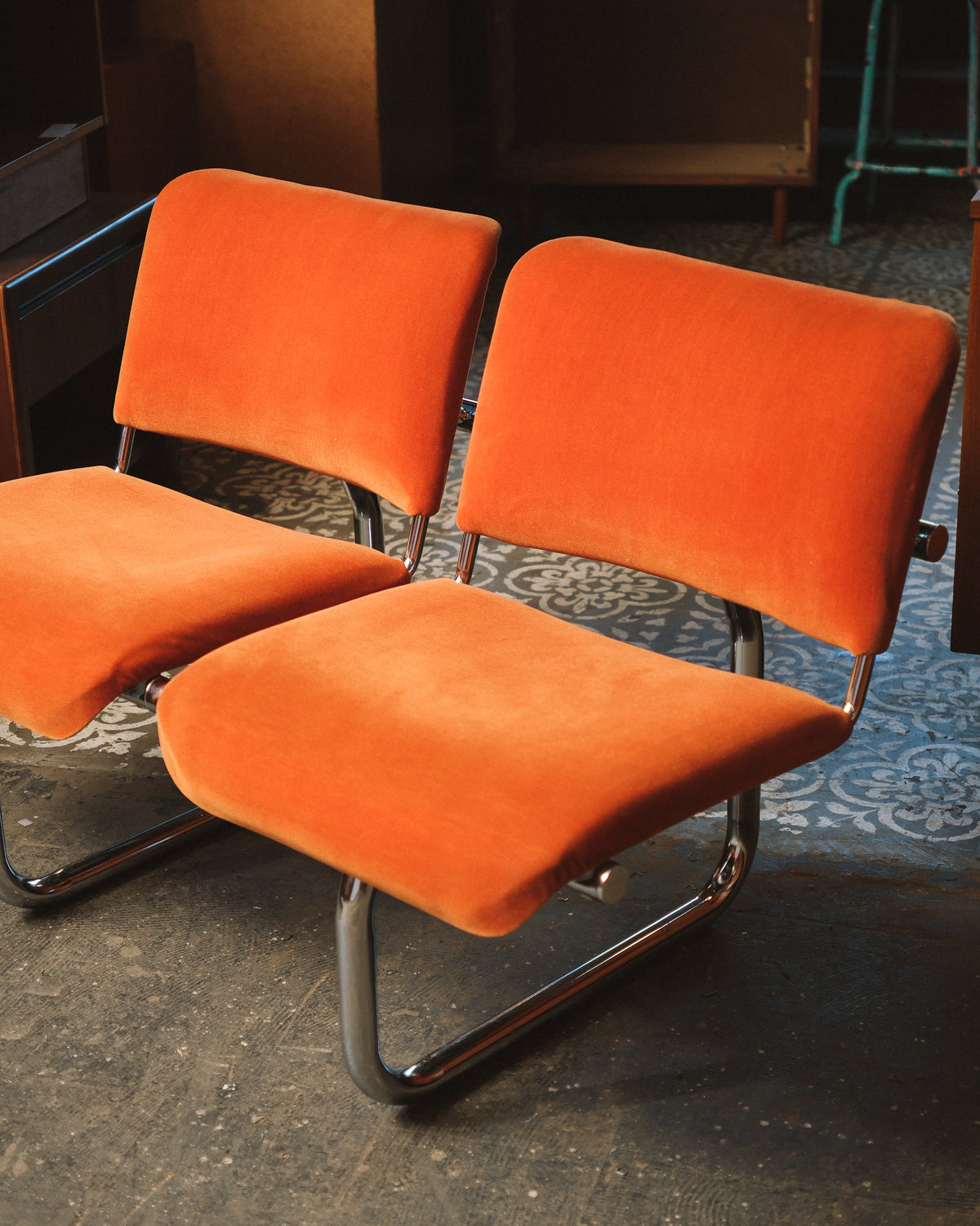 Angled view of two orange tubular chairs showing the cantilevered chrome base.