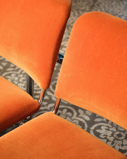 Overhead detail of stacked orange tubular chairs showing chrome frame connections.