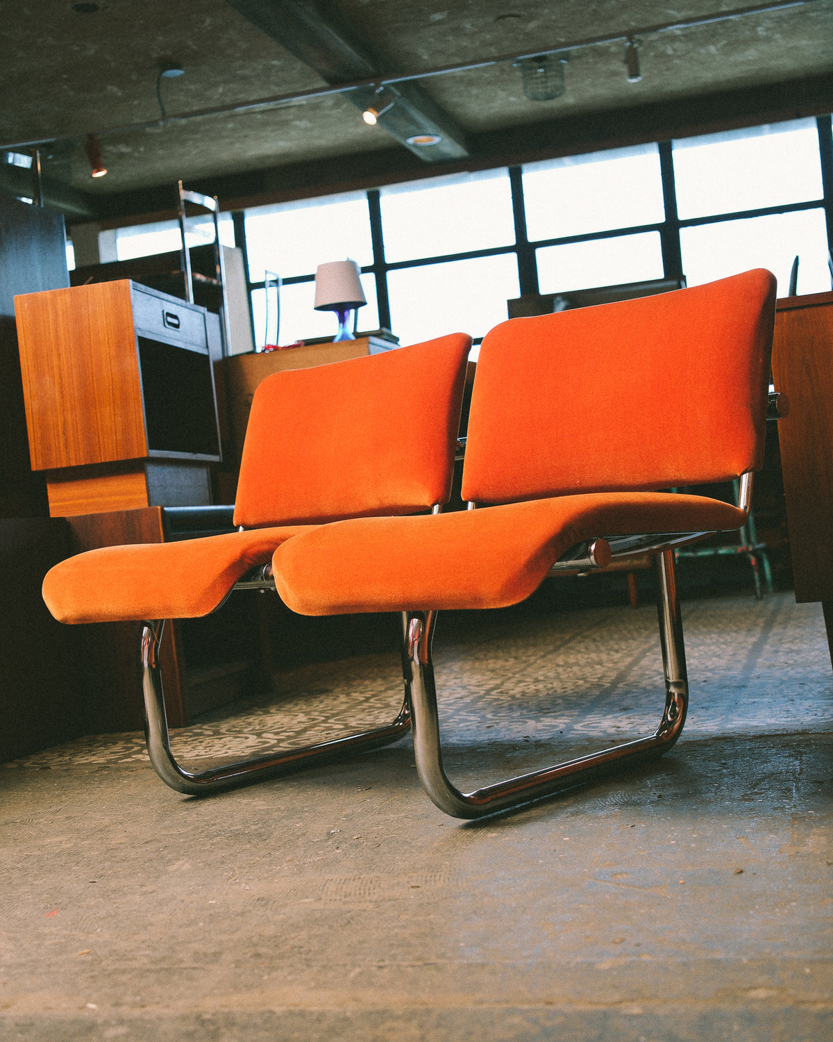 Low angle view of two orange tubular chairs highlighting the curved chrome legs.