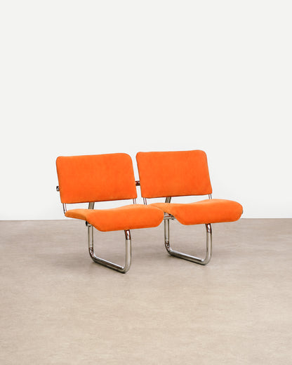 Side profile of an orange tubular chair showing the seat and backrest shape.