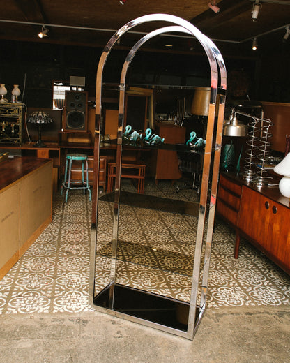 Chrome and smoked glass arched shelving unit displayed in showroom setting among other vintage furniture.