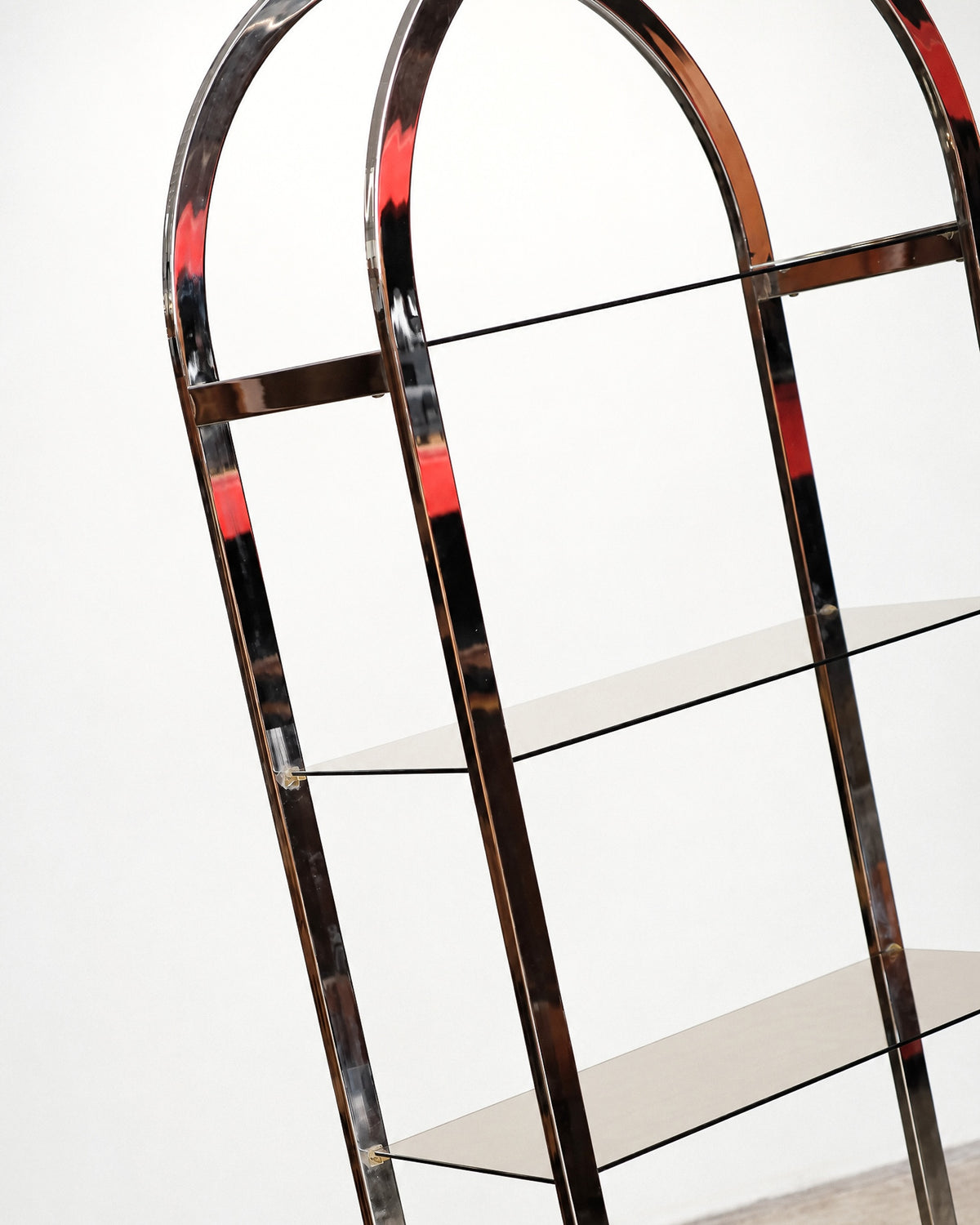 Close-up of the upper arched chrome frame showing glass shelf brackets and joinery detail.