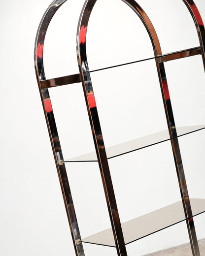 Close-up of the upper arched chrome frame showing glass shelf brackets and joinery detail.