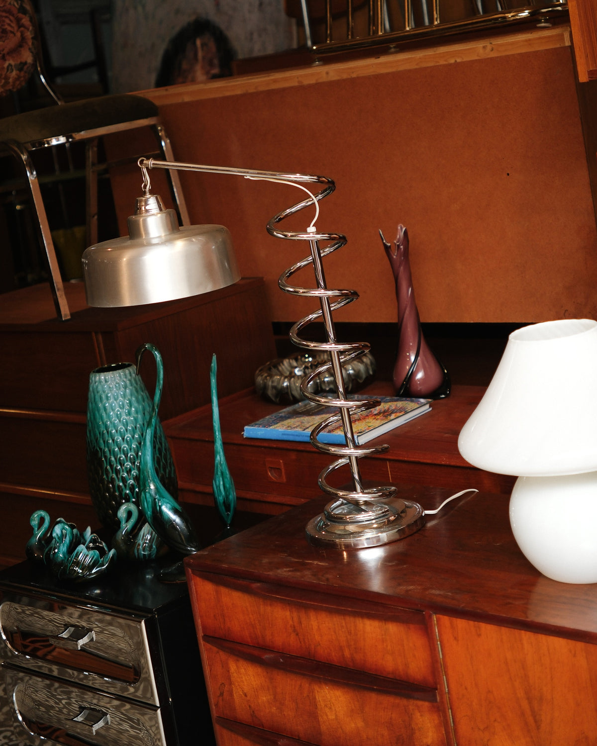 Chrome spiral table lamp displayed on a wood cabinet among vintage decor and glassware