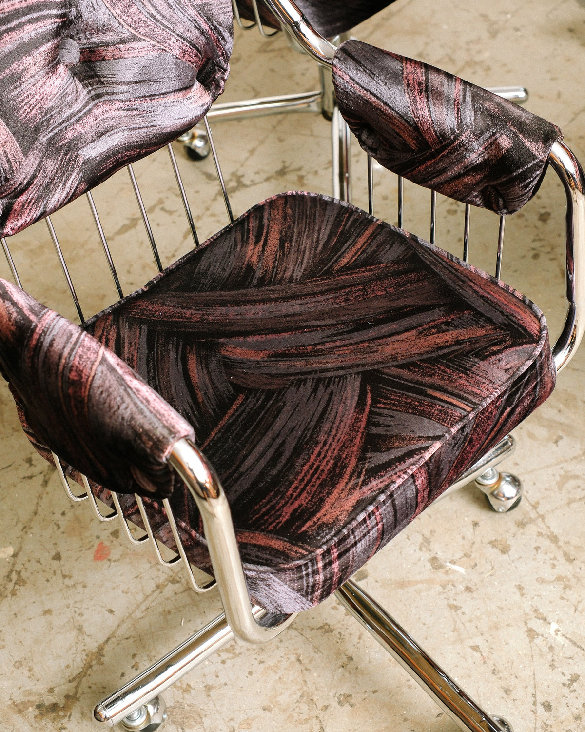 Close-up angled view of chrome swivel armchair showing patterned upholstery on seat and armrests