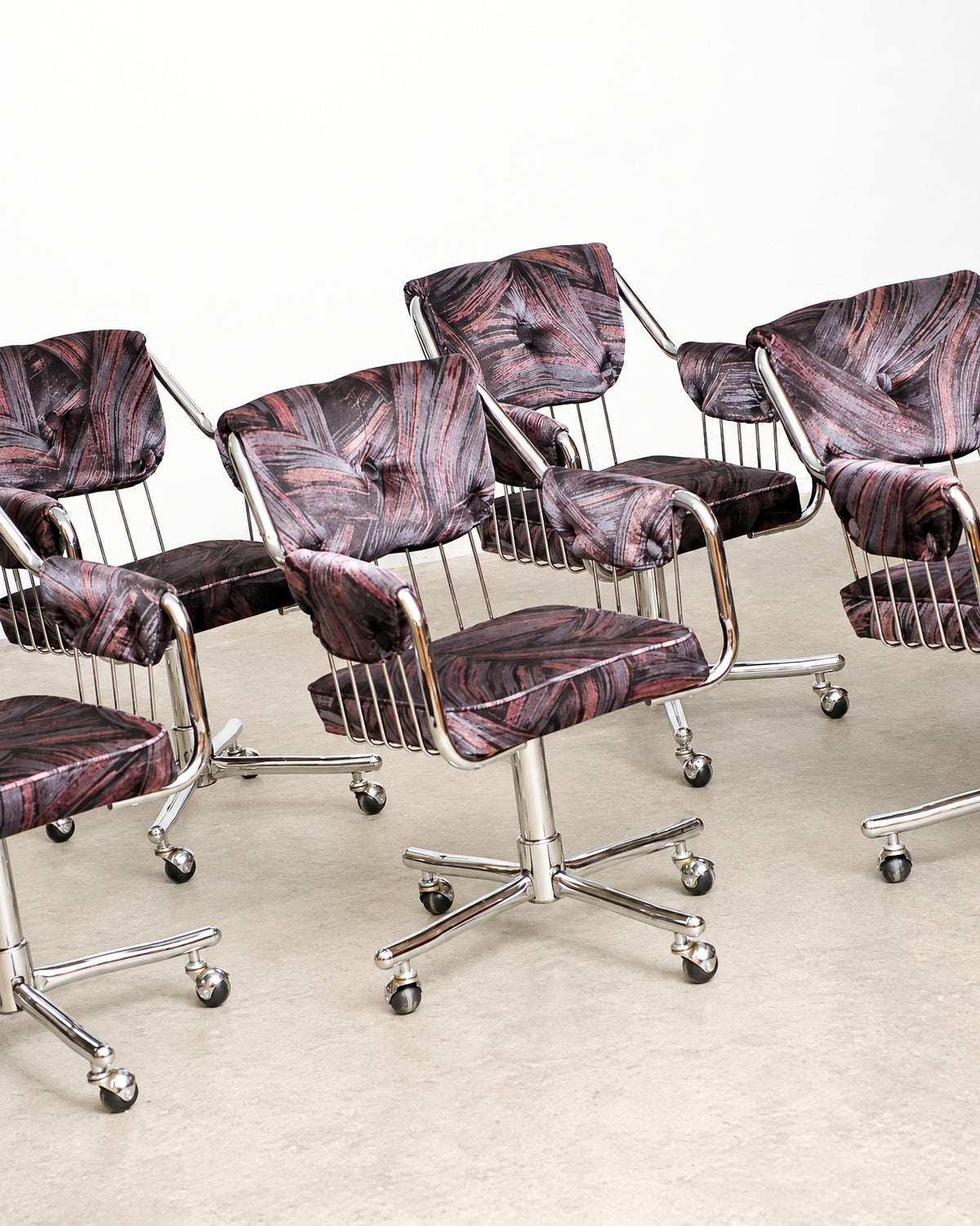 Angled view of four chrome swivel armchairs on a plain background showing full chair profiles