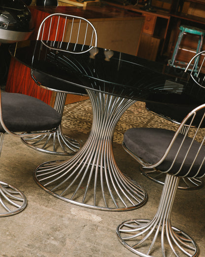 Close angle on the radiating chrome pedestal base beneath the oval glass table top.