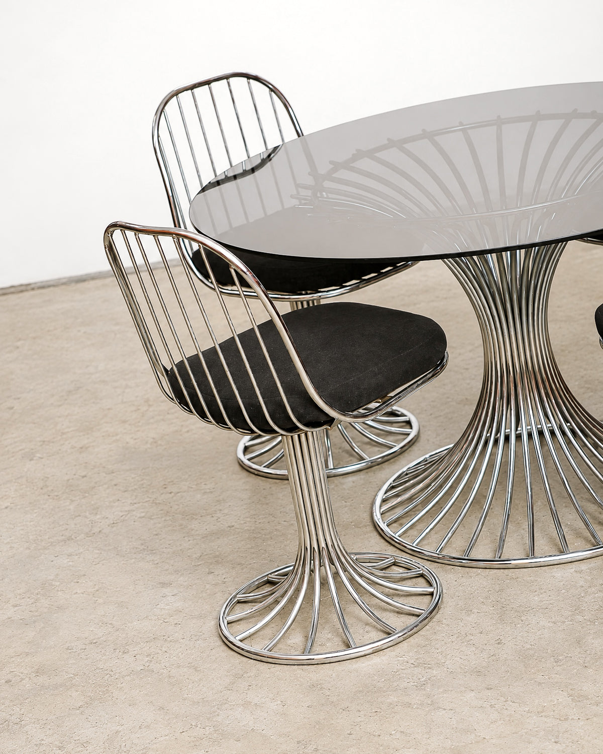 Angled view of two chairs and the table showing the chrome wire base and glass top reflection.