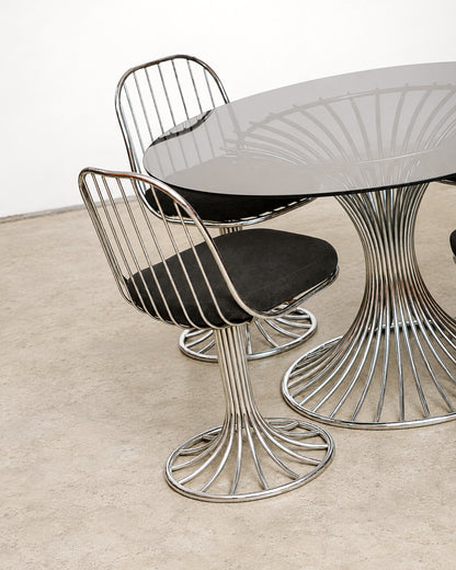 Angled view of two chairs and the table showing the chrome wire base and glass top reflection.