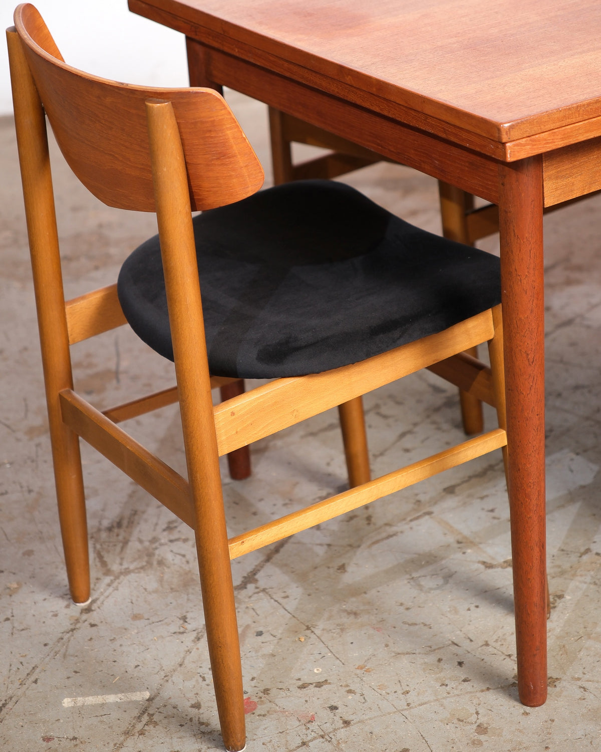 Close-up of a chair back and seat beside the teak dining table leg and apron.