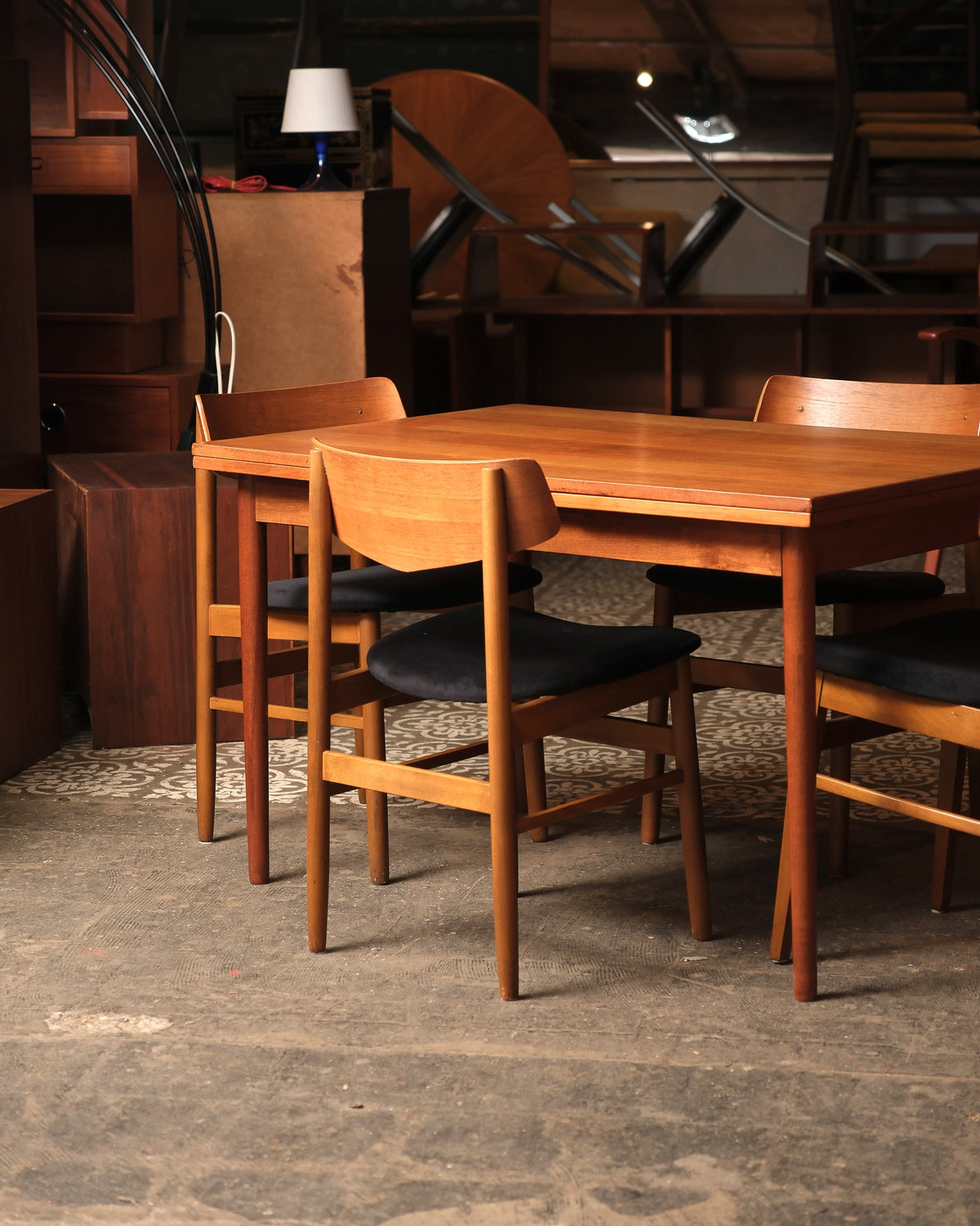 Angled view of the table and chairs in the showroom with additional teak furniture in the background.