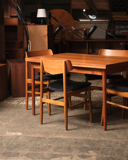 Angled view of the table and chairs in the showroom with additional teak furniture in the background.