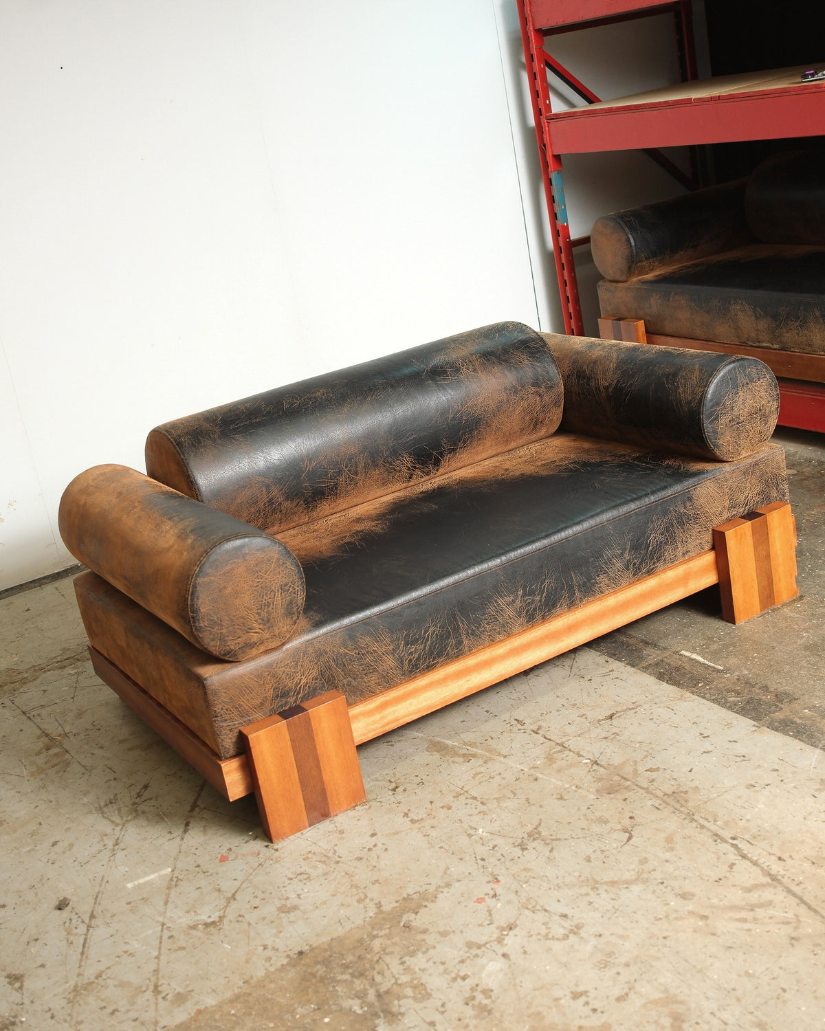 Distressed dark leather sofa with bolster arms and backrest, shown at an angle against a white wall.