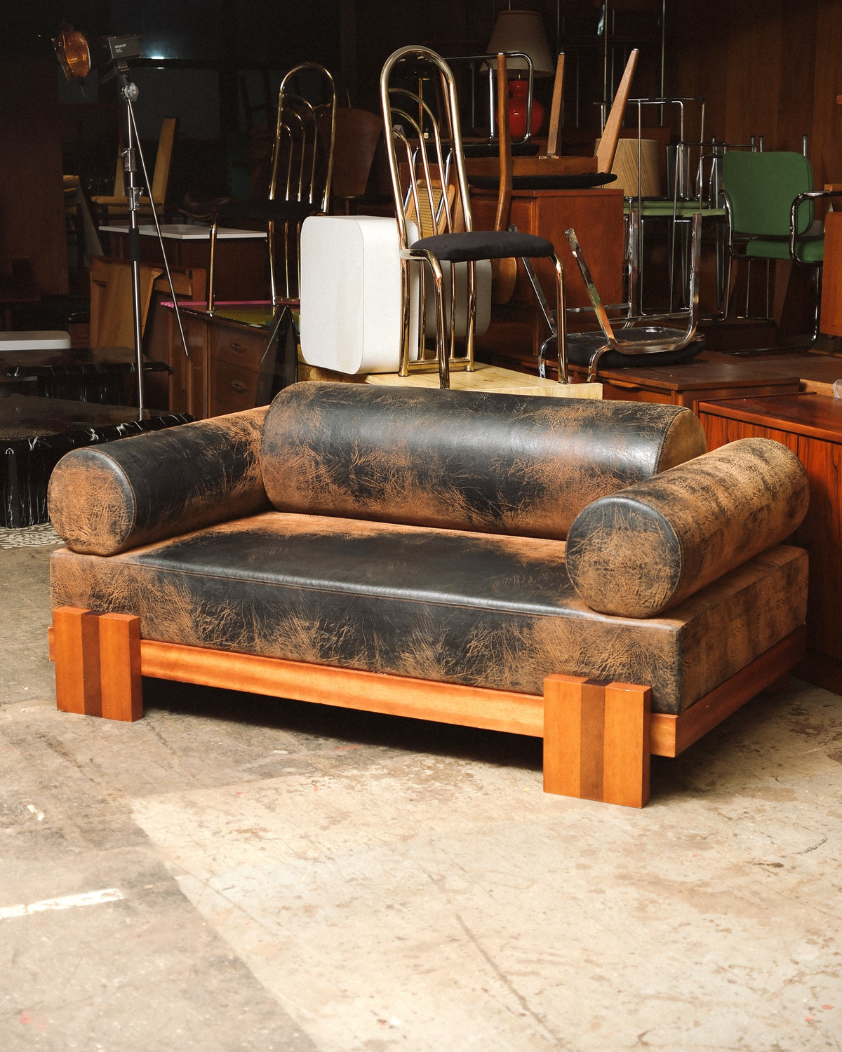 Front view of distressed dark leather sofa with wood block feet, shown in a furniture showroom.