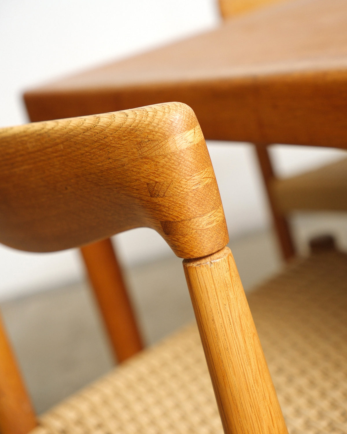 Detail of a chair's back rail joint and leg, with the extension table visible behind.