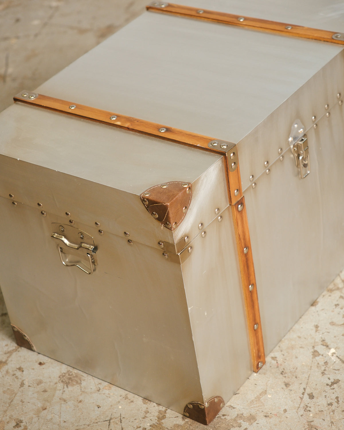 Corner view of the large industrial trunk showing wood banding, leather corner guards, and riveted metal cladding.