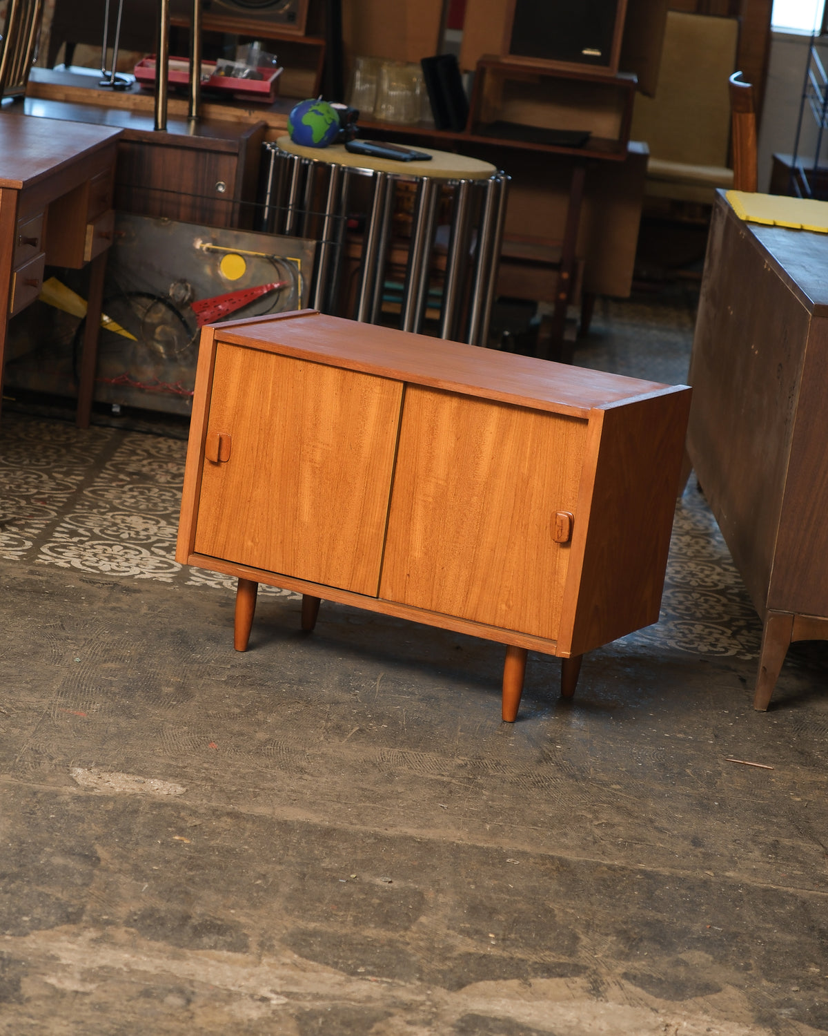 Angled view of a mid-century modern Danish teak cabinet with sliding doors and tapered legs, shown in a furniture showroom.