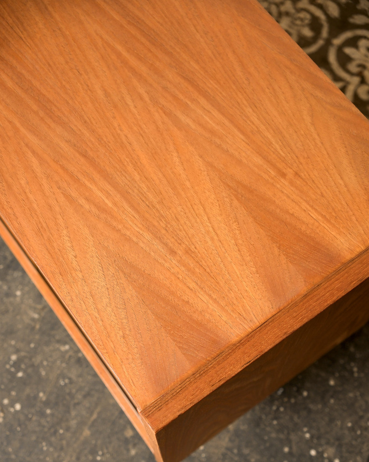 Close-up of the teak cabinet's top surface showing natural wood grain and mitred corner detail.