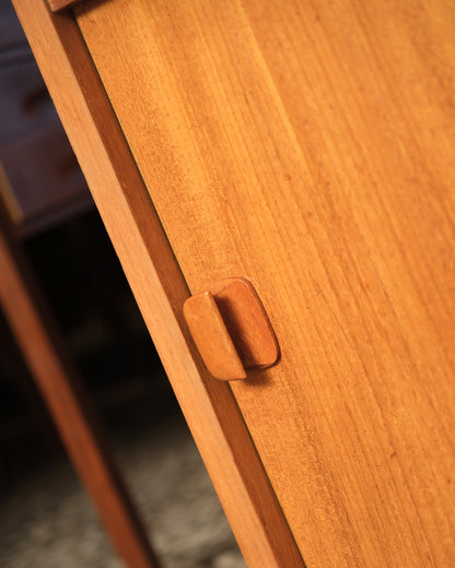 Close-up of the sculpted wood door pull and sliding door seam on the teak cabinet.
