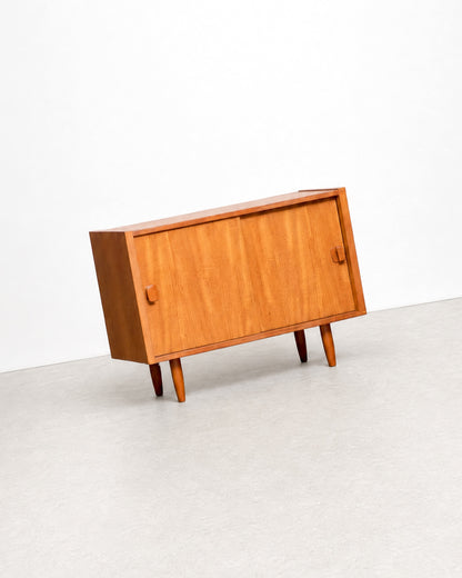 Side angle view of the teak cabinet against a plain white background, showing its tapered legs.
