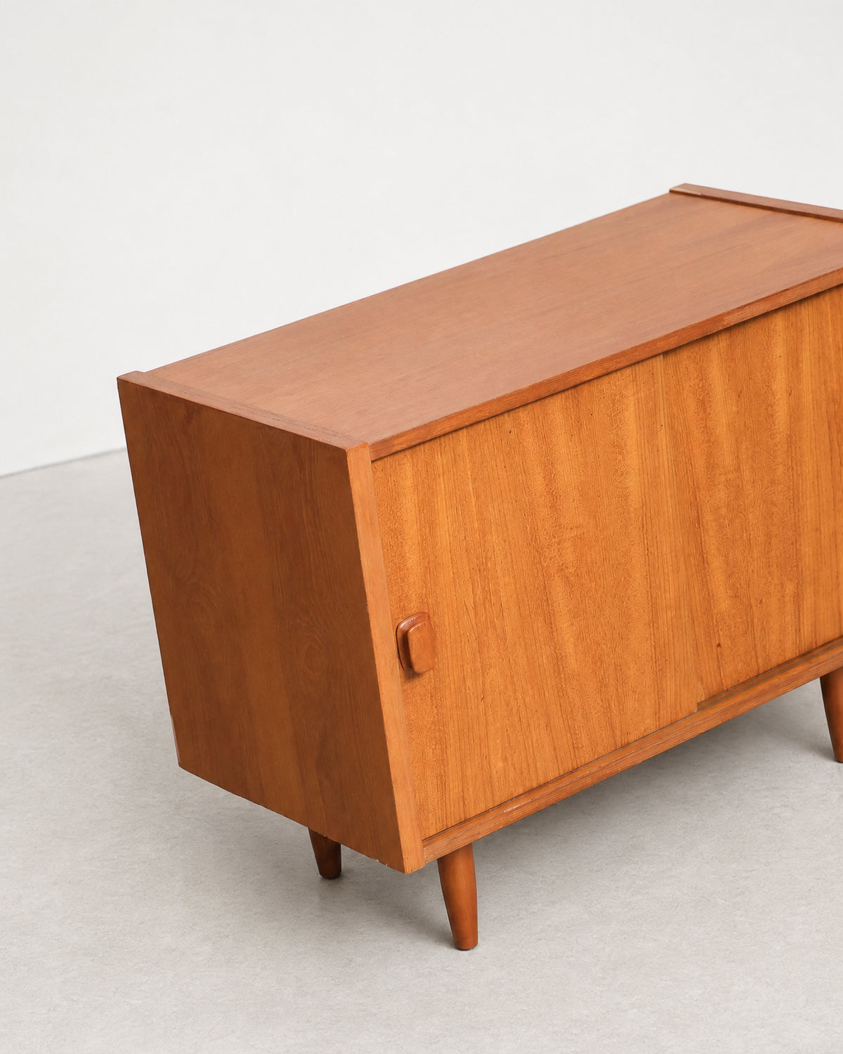 Close-up angled view of the teak cabinet's side panel, door pull, and tapered leg.