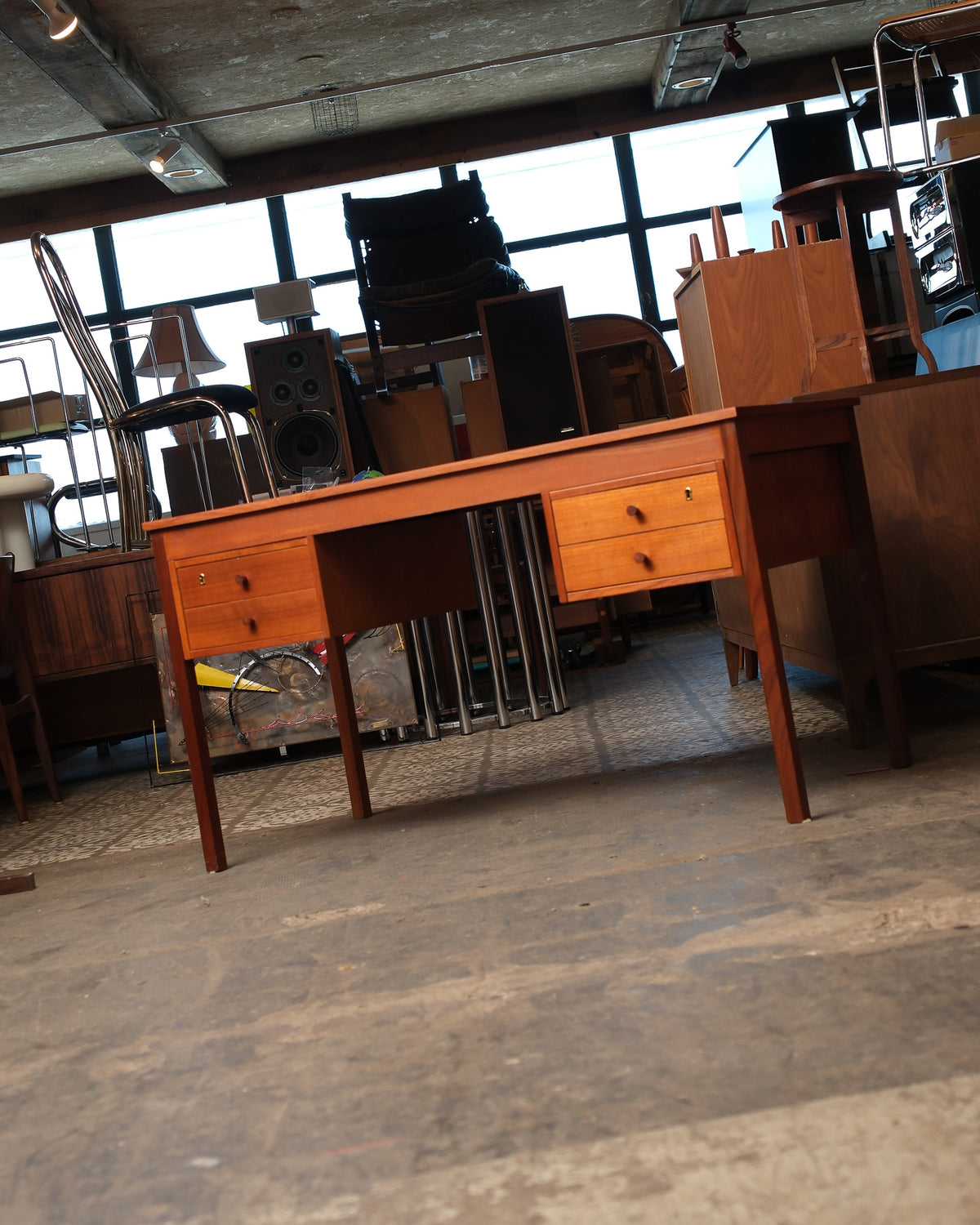 Full side view of the teak desk showing tapered legs and drawer bank, set among other pieces.