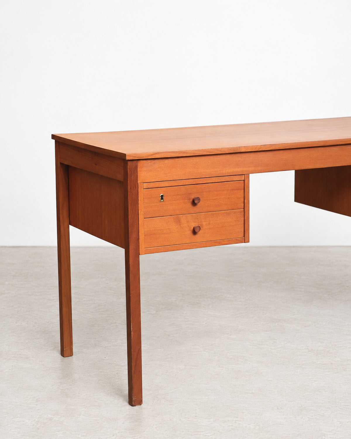 Side profile of the desk highlighting the tapered leg and clean teak lines in studio light.