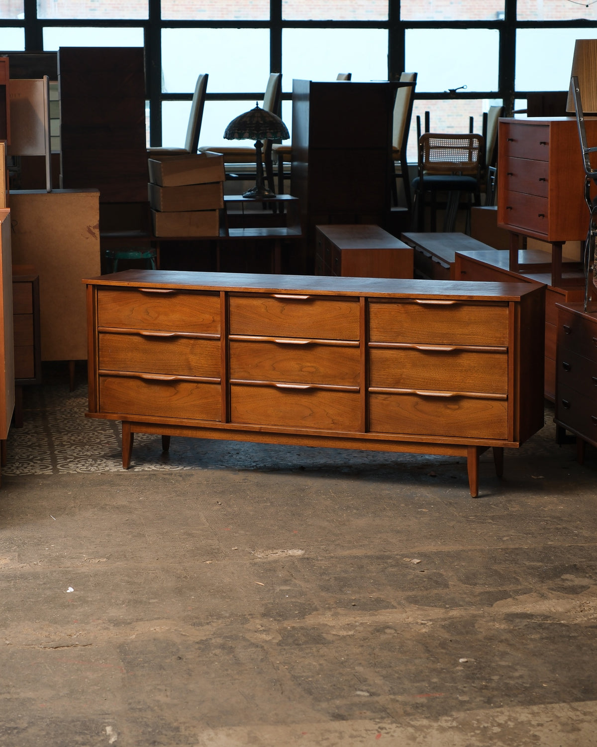 Front view of the mid-century modern dark walnut 9-drawer dresser in a warehouse setting