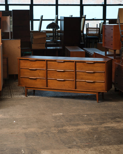 Front view of the mid-century modern dark walnut 9-drawer dresser in a warehouse setting