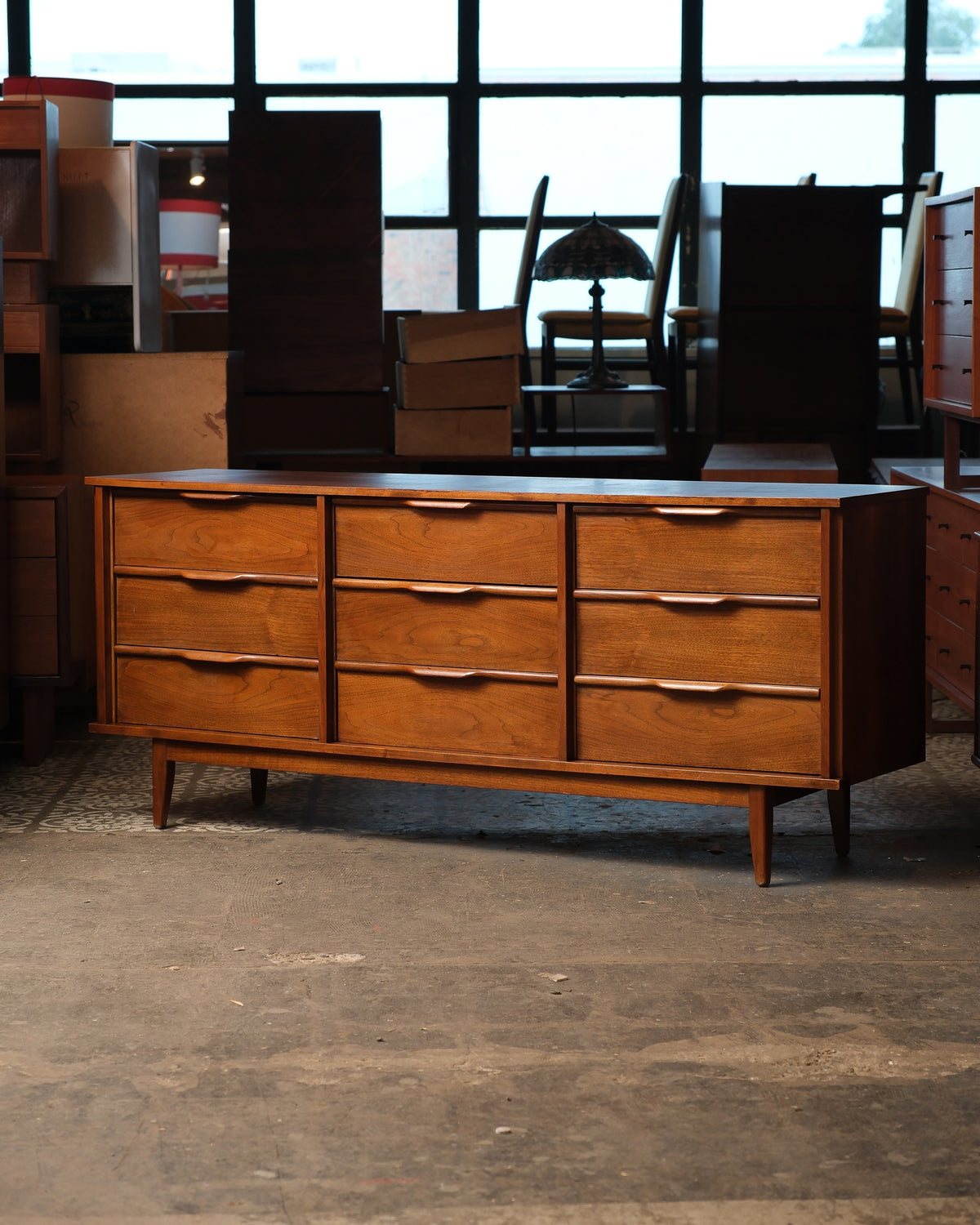 Front view of the dresser against a warehouse window with other furniture in background
