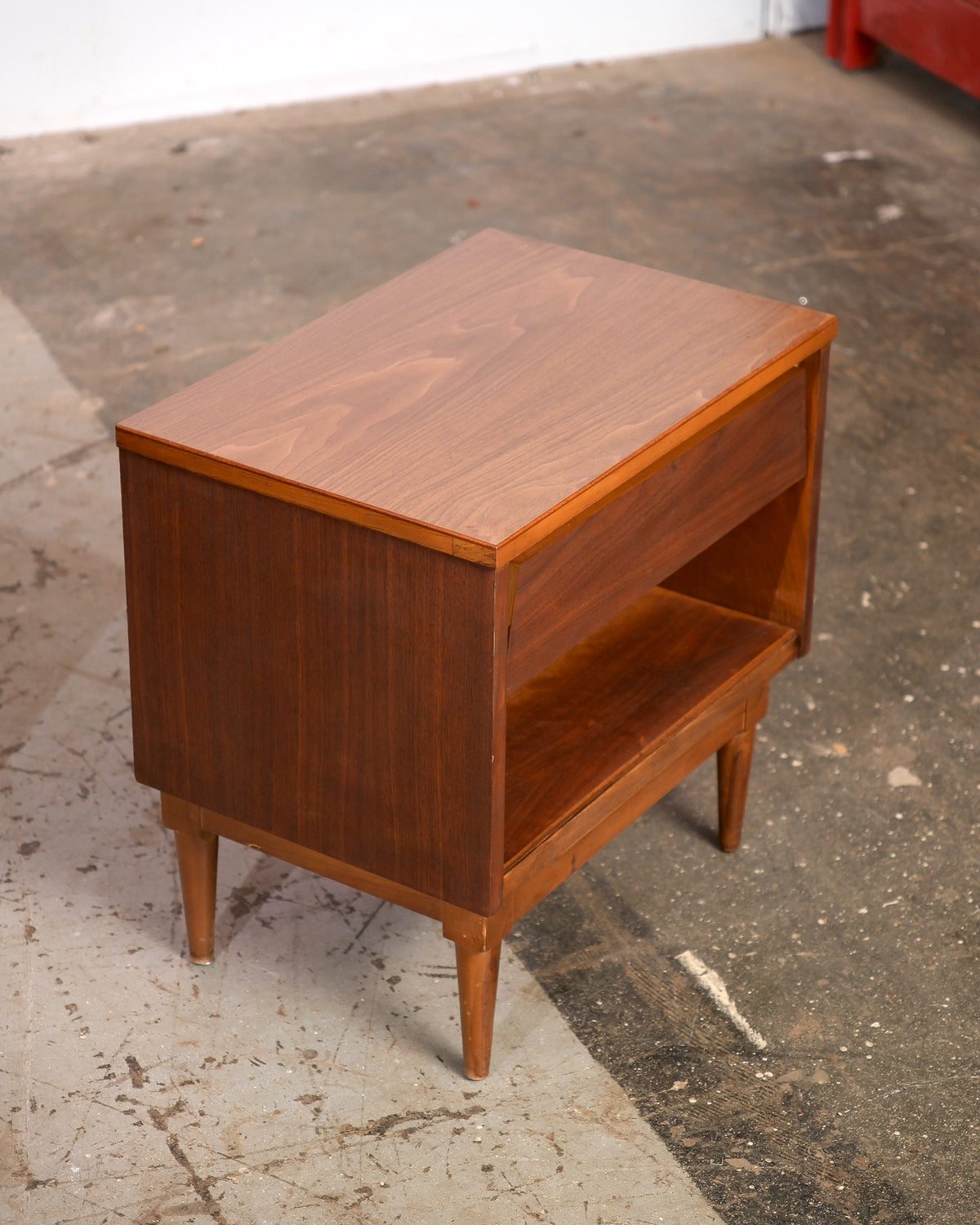 Angled overhead view of a mid-century modern dark walnut nightstand showing the drawer front and open lower shelf.