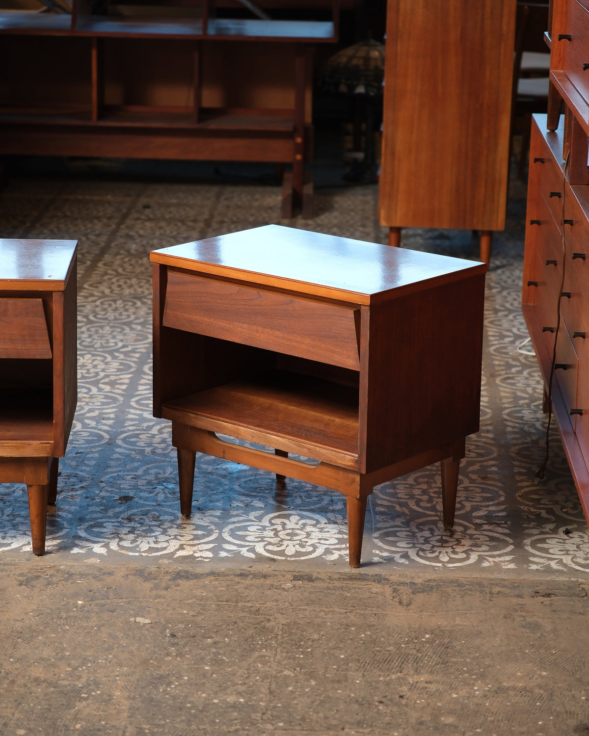 Front view of a single mid-century modern dark walnut nightstand with tapered legs and sculpted stretcher.