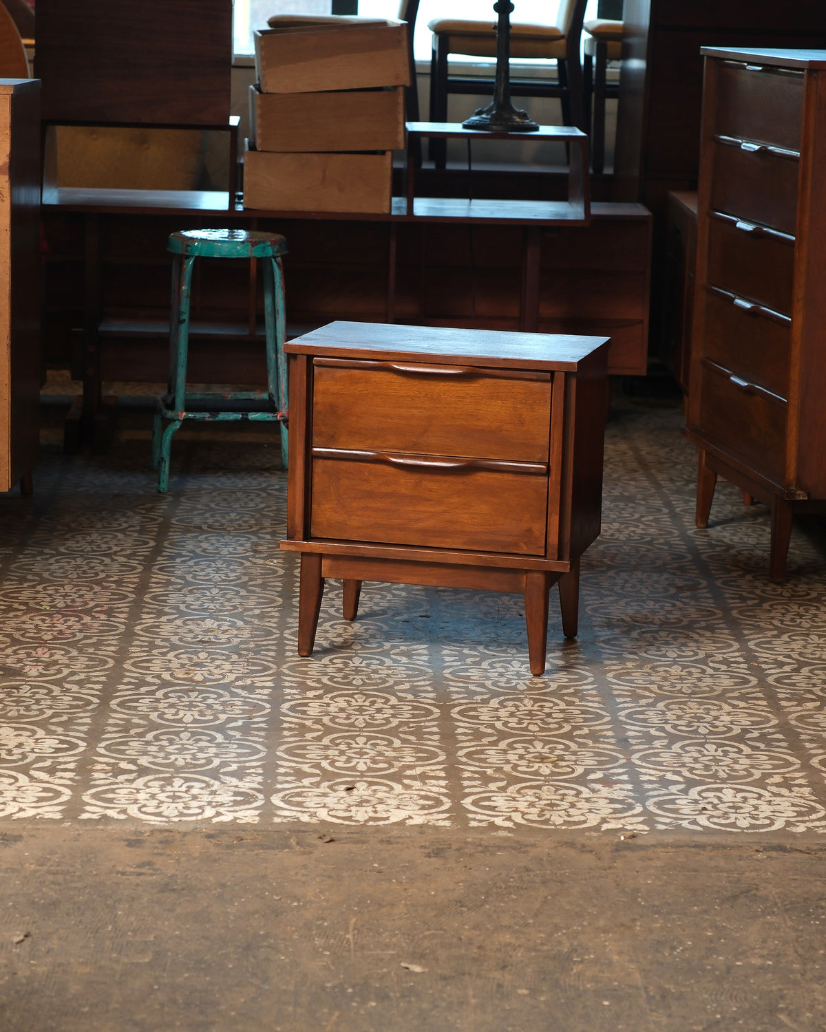 Mid-century modern dark walnut nightstand with two drawers, shown in a showroom setting.