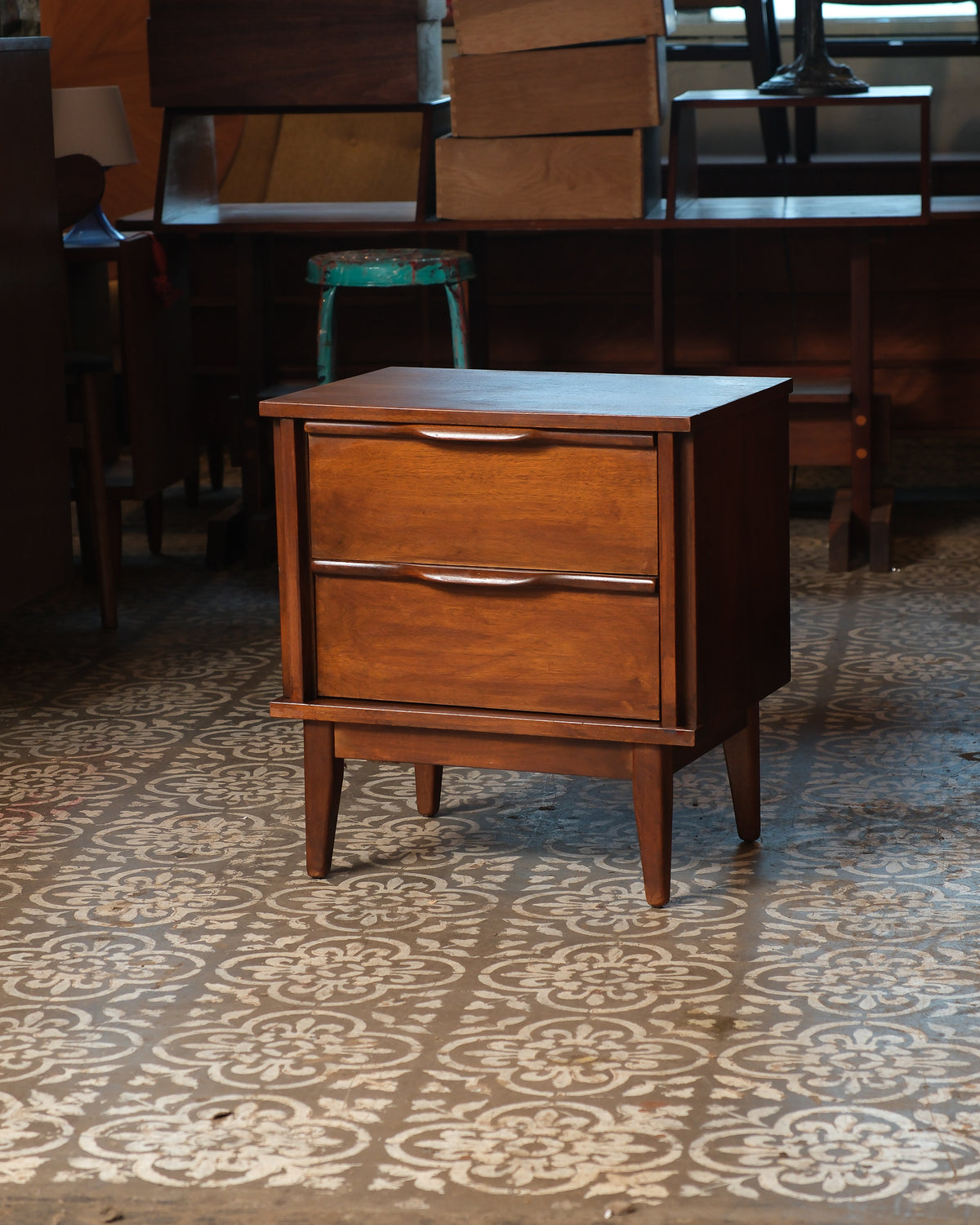 Front angle view of the walnut nightstand showing sculpted drawer pulls and tapered legs.