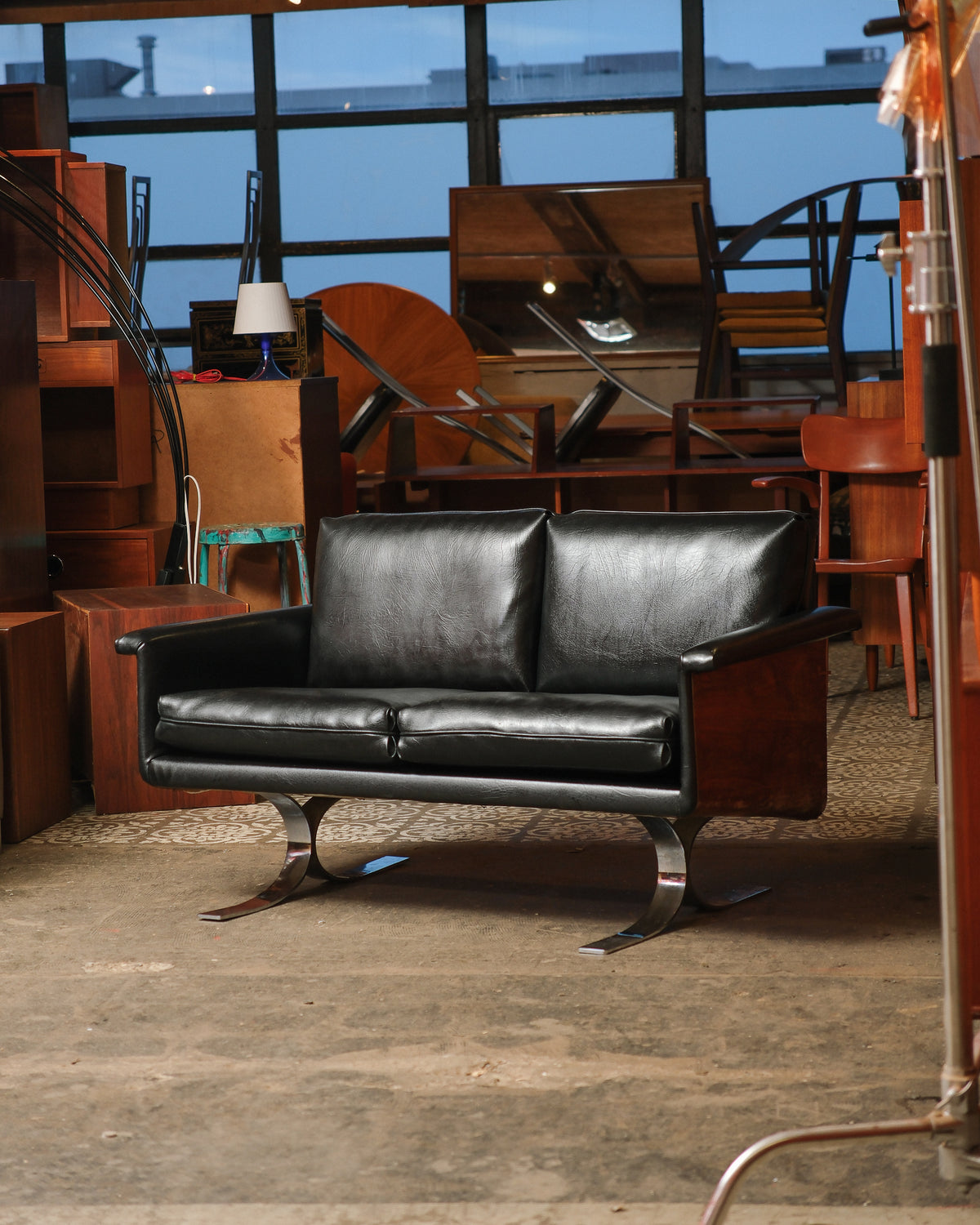 Mid-century modern leather sofa with chrome legs and wood side panels, shown in a warehouse setting.