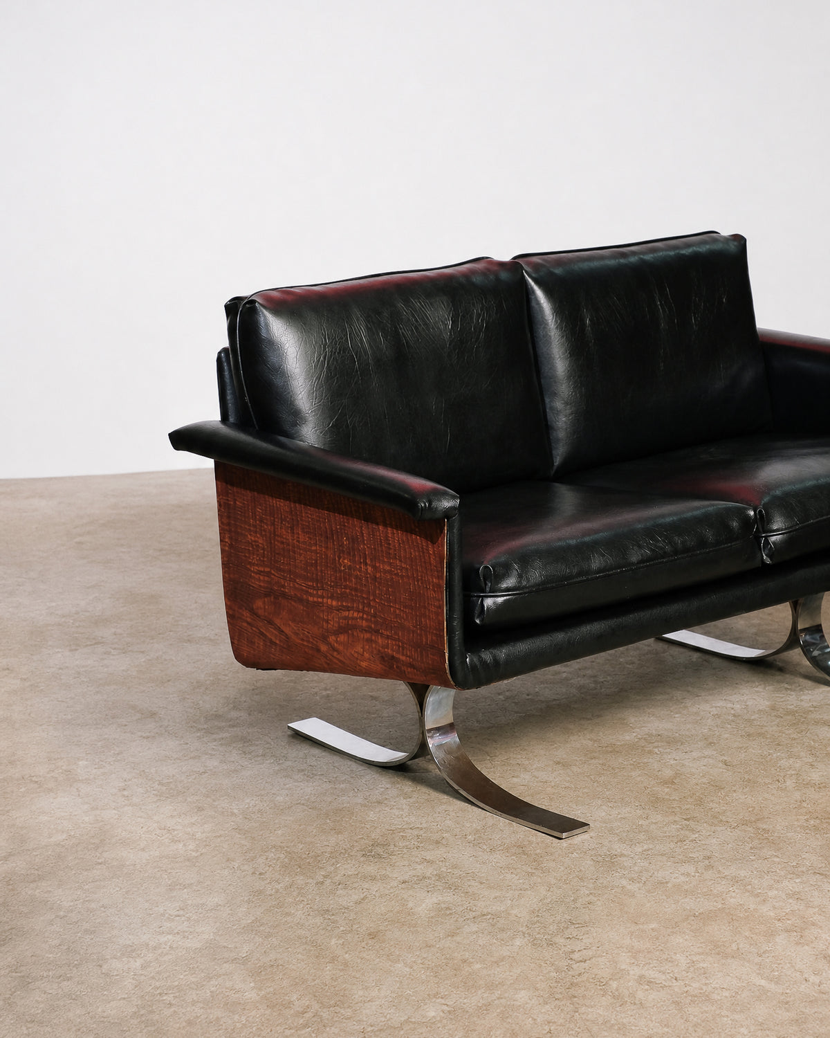 Side view of the sofa highlighting the curved wood panel and sculptural chrome leg.