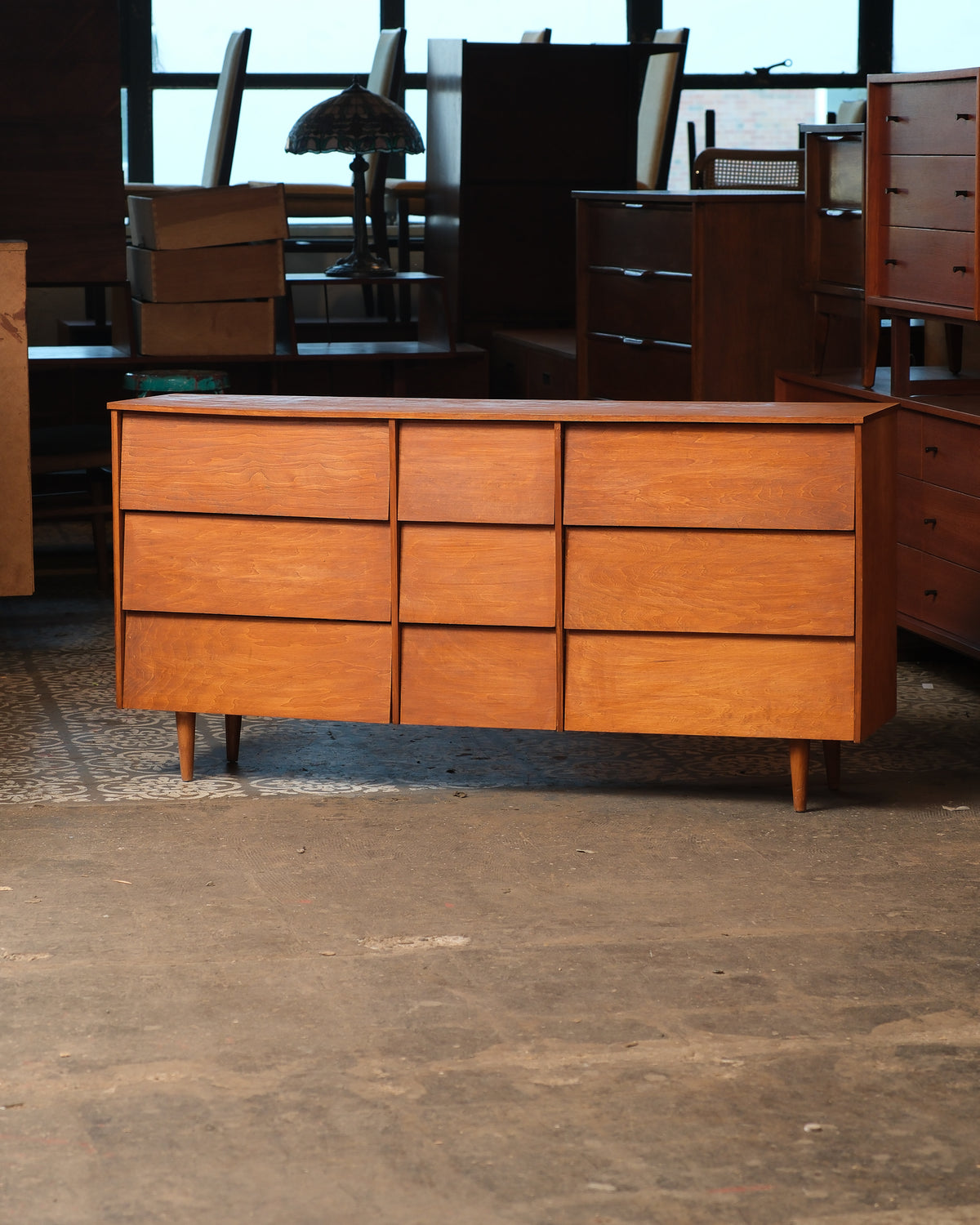 Mid-century modern maple 9-drawer dresser shown straight-on in a furniture showroom.