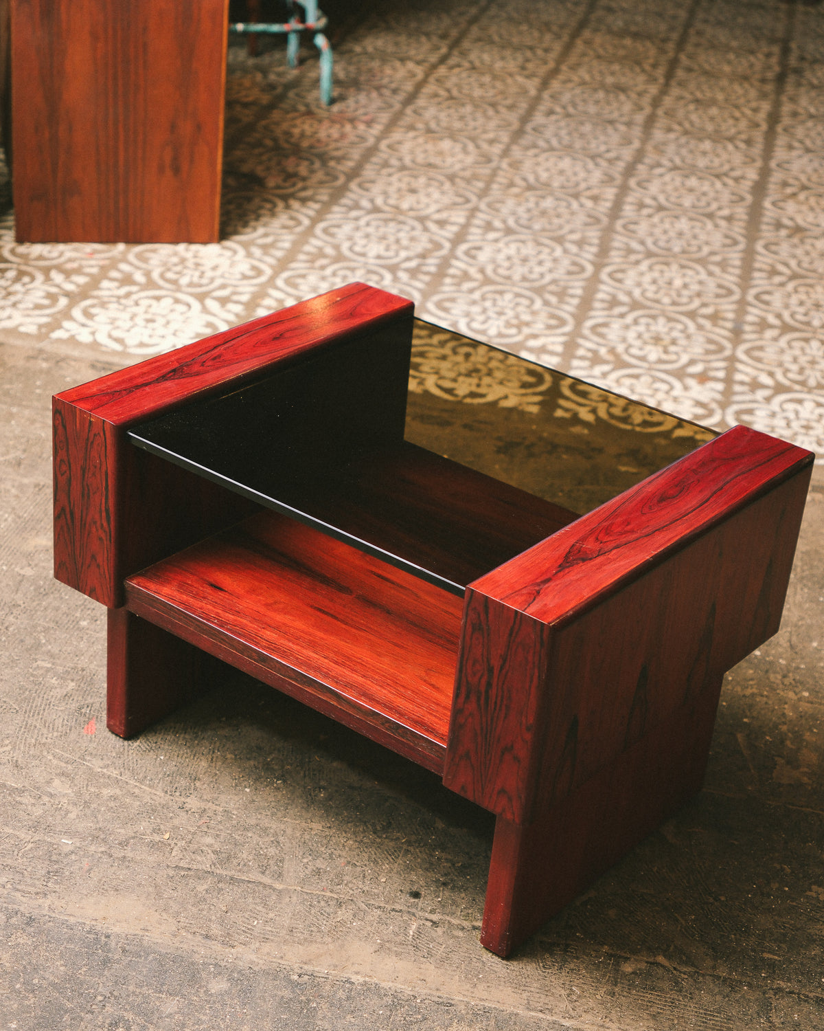 Three-quarter view of the rosewood coffee table showing the open shelf and glass top.