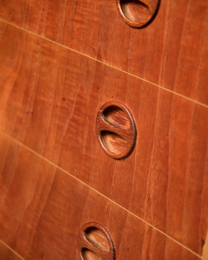 Close-up of a carved oval teak drawer pull showing wood grain detail.