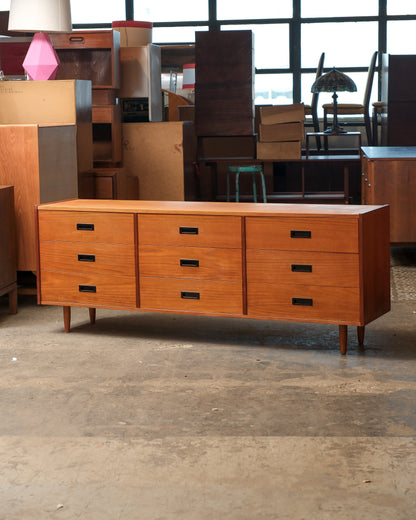 Straight-on front view of the teak 9-drawer dresser in a warehouse setting