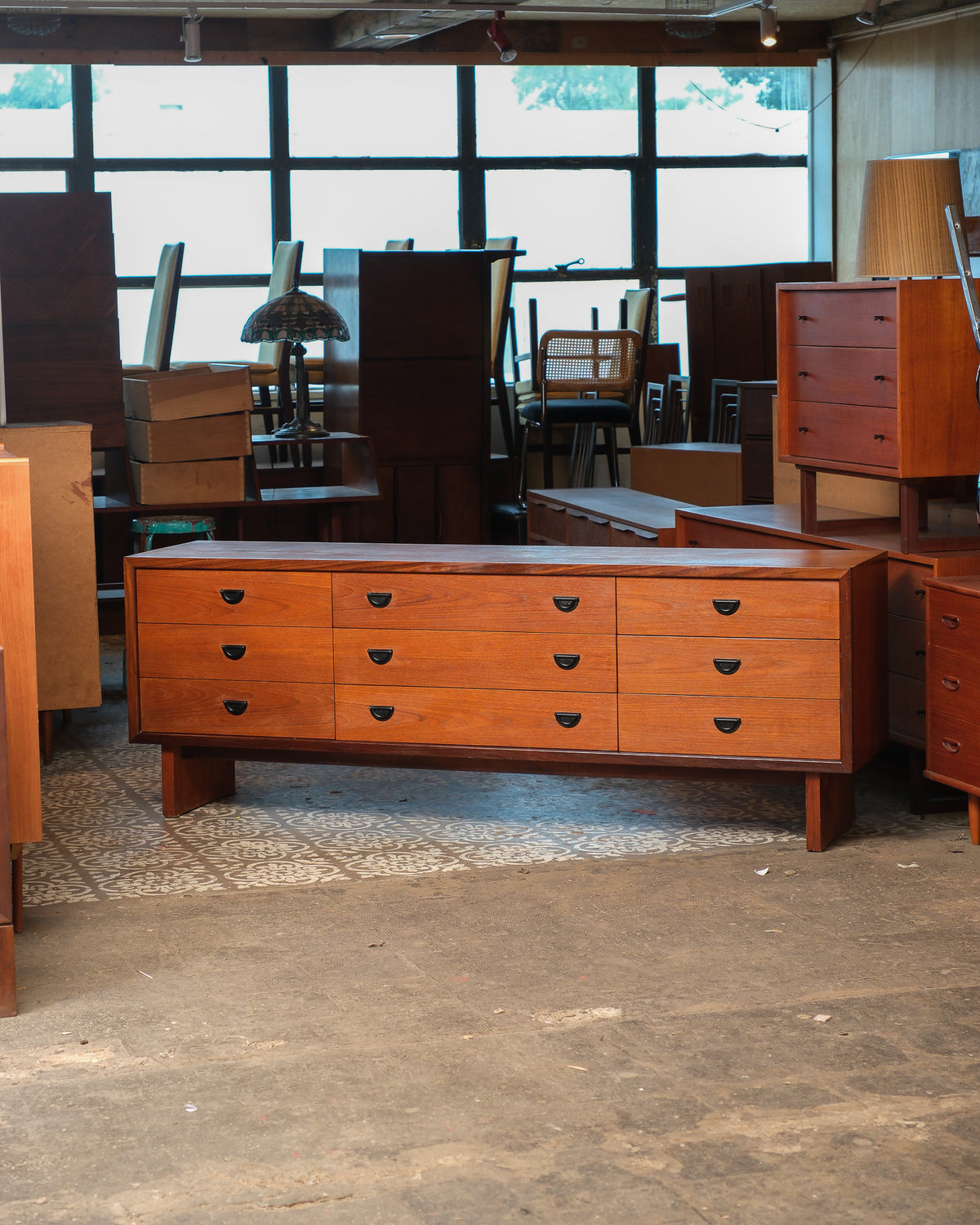 Mid-century modern teak 9-drawer dresser shown from the front in a warehouse setting.