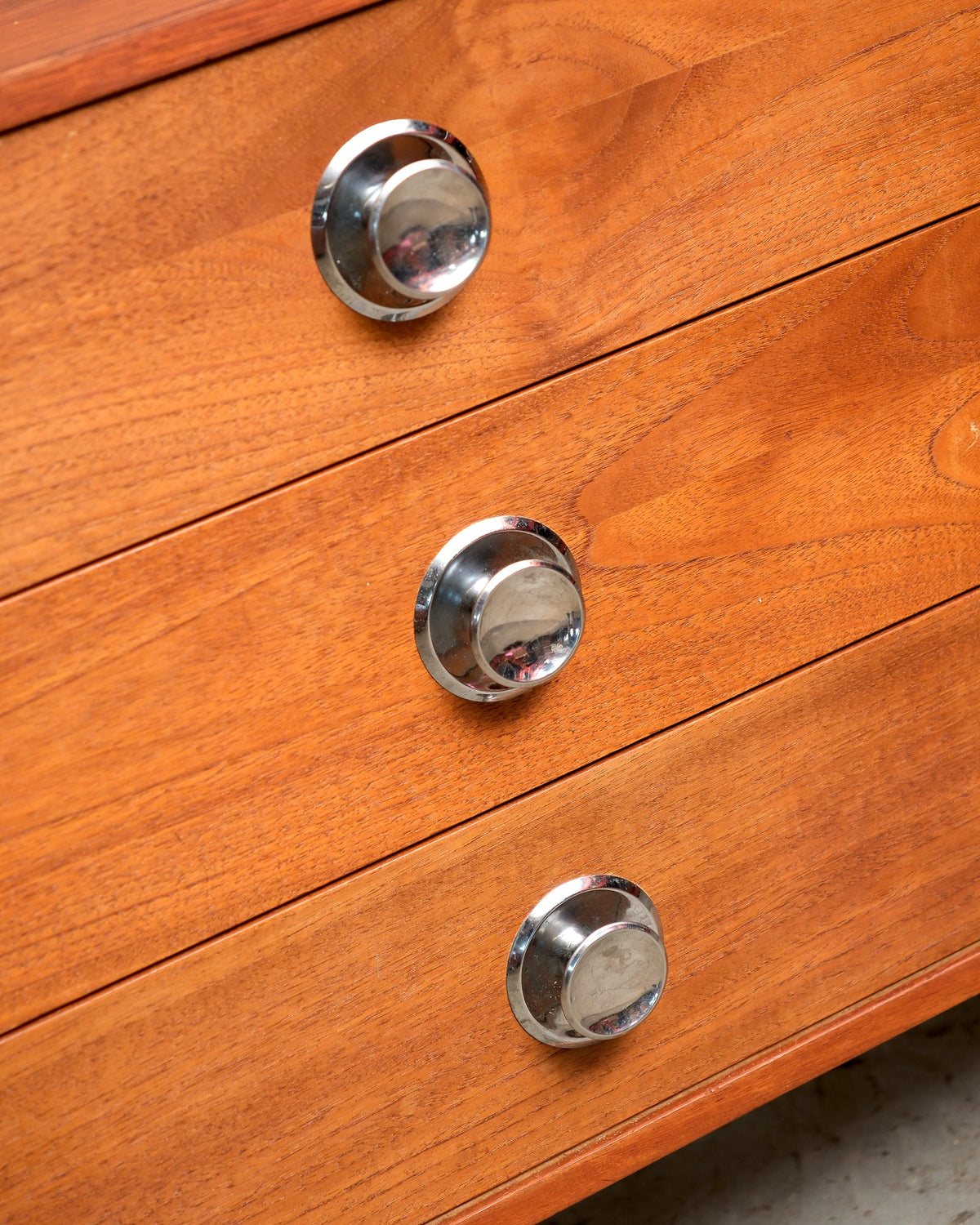 Close-up of two round chrome knobs on teak drawer fronts, showing wood grain detail.