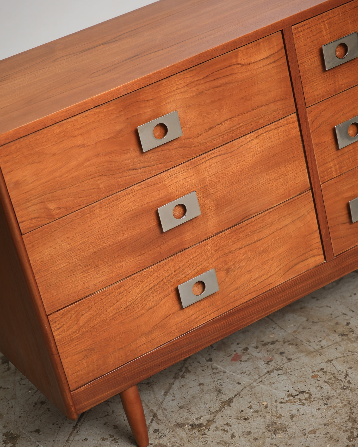 Angled view of the drawer front grouping with squared chrome knob pulls and tapered leg visible.