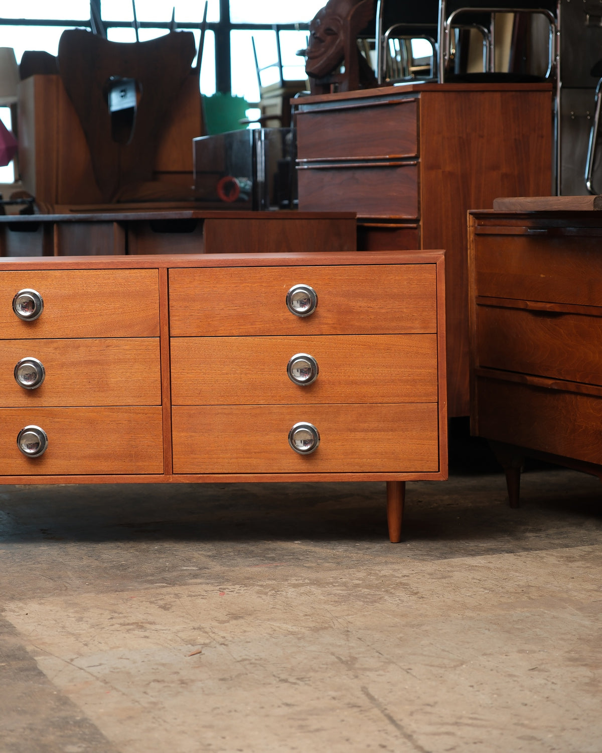 Front view of the teak 9-drawer dresser shown alongside other vintage furniture in the shop.