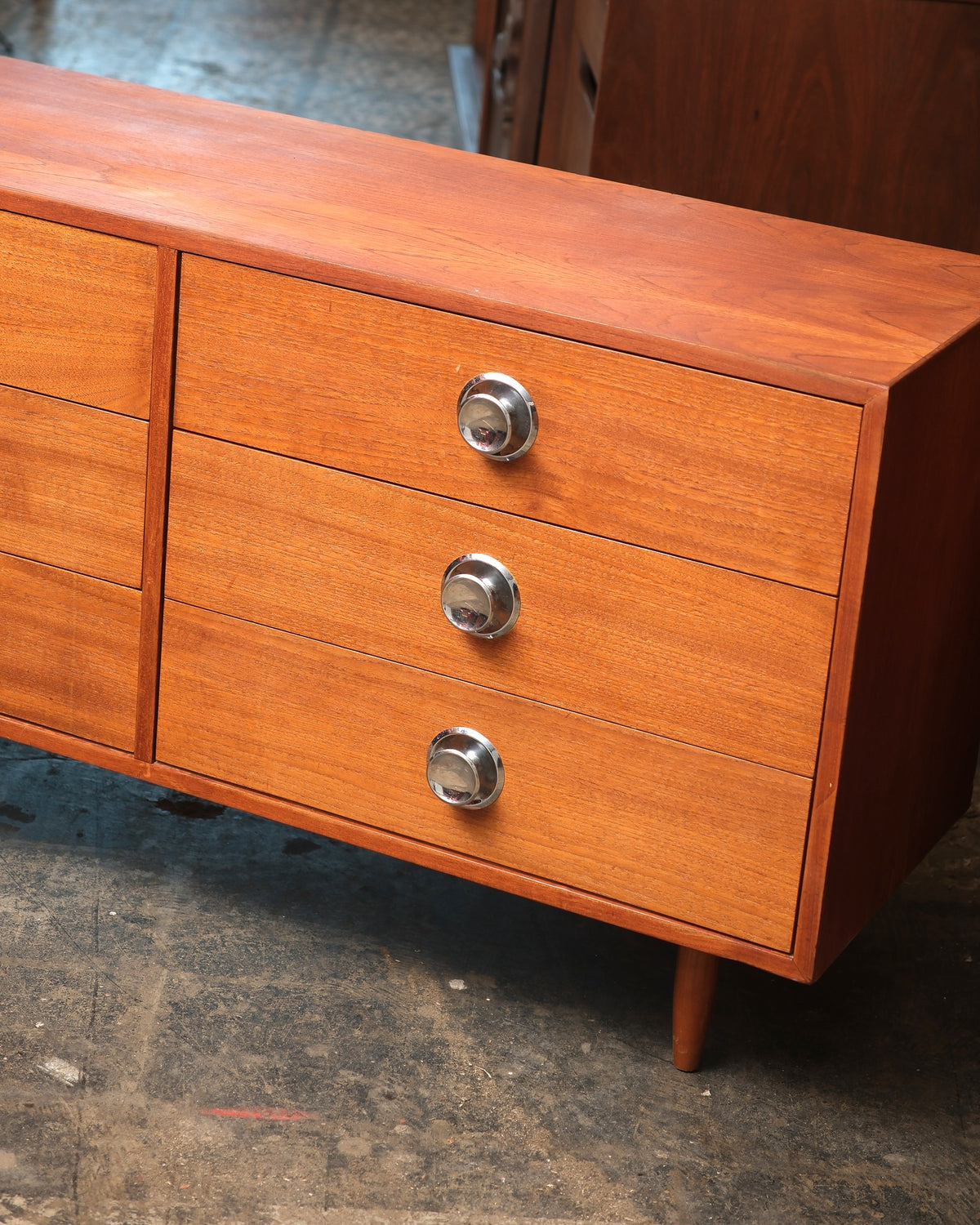 Angled view of the dresser's right side showing three drawers with chrome knobs and a tapered leg.