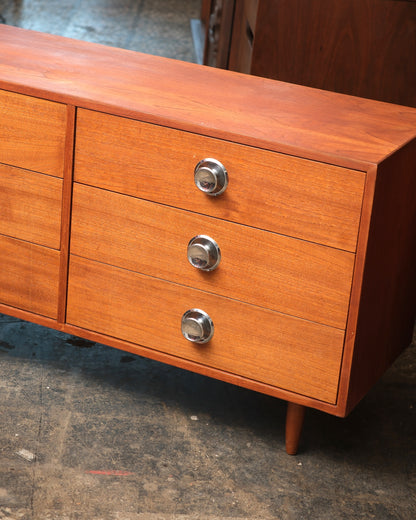 Angled view of the dresser's right side showing three drawers with chrome knobs and a tapered leg.