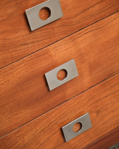 Close-up of three chrome knob pulls set against the teak drawer fronts.