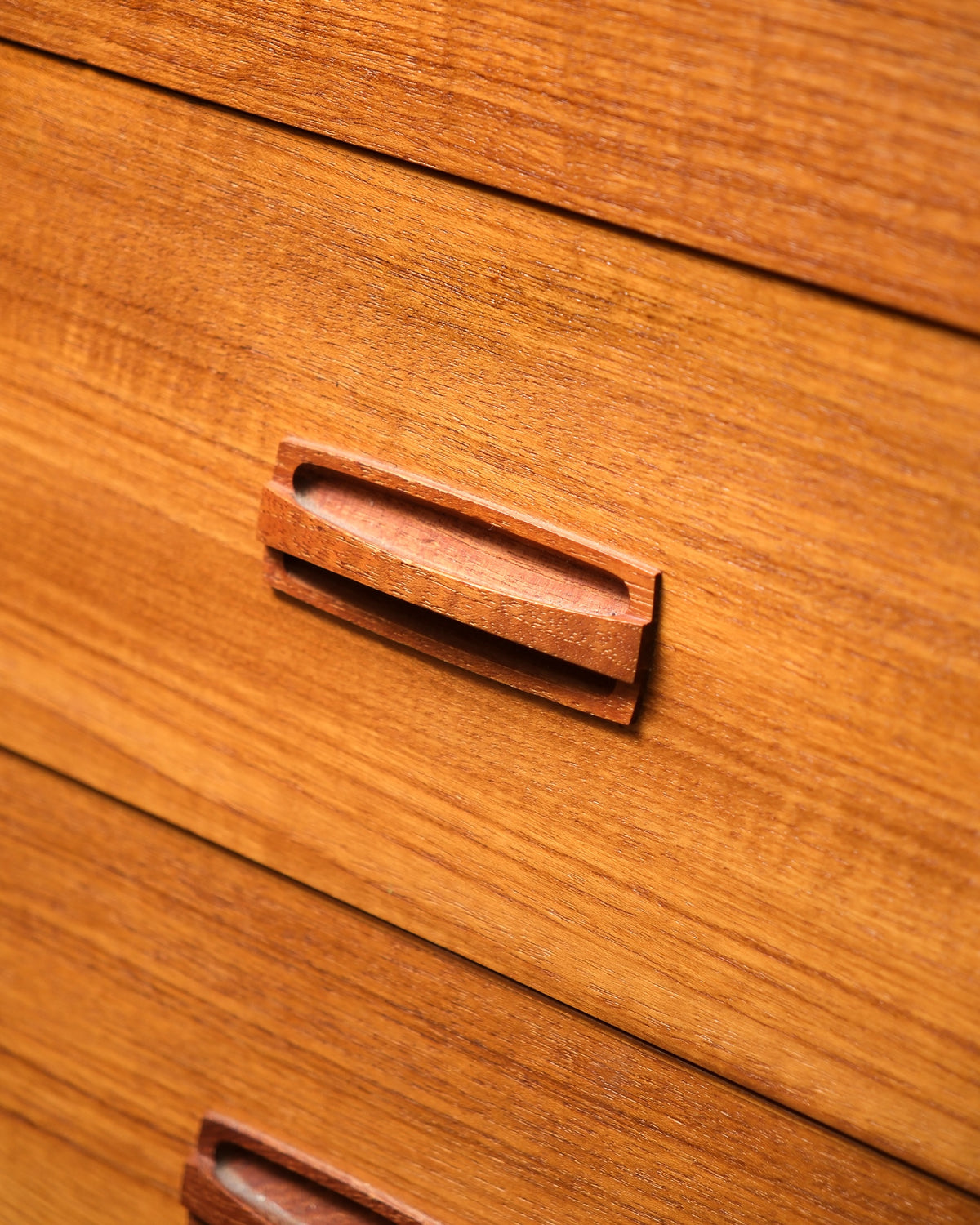Close-up of a sculpted teak drawer pull showing the wood grain and carved shape.
