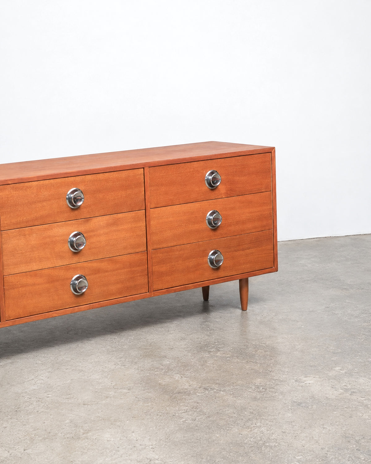 Side view of the dresser showing six drawers, chrome knobs, and tapered wood legs.